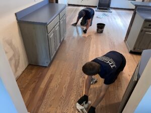 Two people cleaning the wooden floor of a house