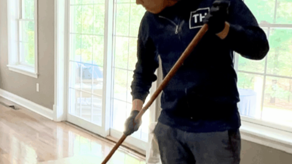 Professional applying finish to hardwood floors in a sunlit living room, demonstrating the secret to achieving a flawless hardwood finish.