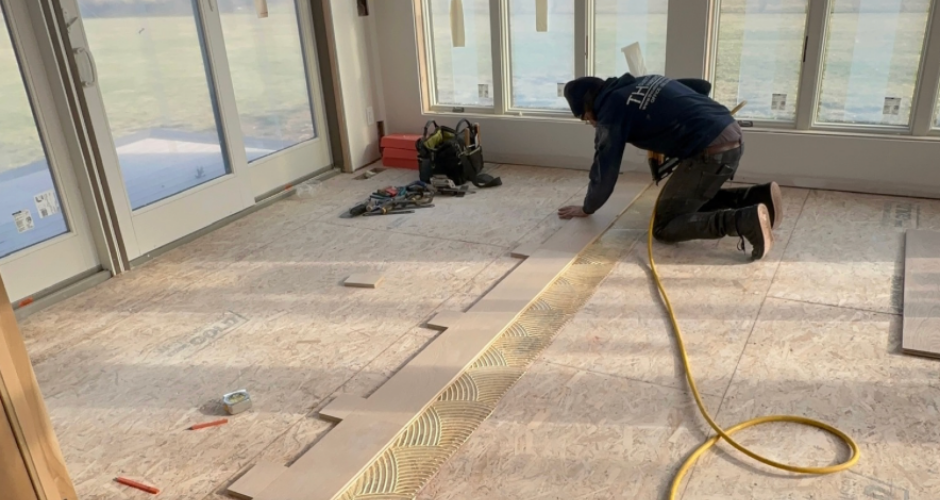 Craftsman from TH Custom Hardwood installing wide-plank flooring, carefully aligning each board over freshly applied adhesive in a sunlit room.