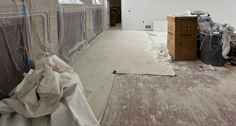 Room under renovation with protective coverings, exposed subflooring, and construction materials prepared for new hardwood installation.