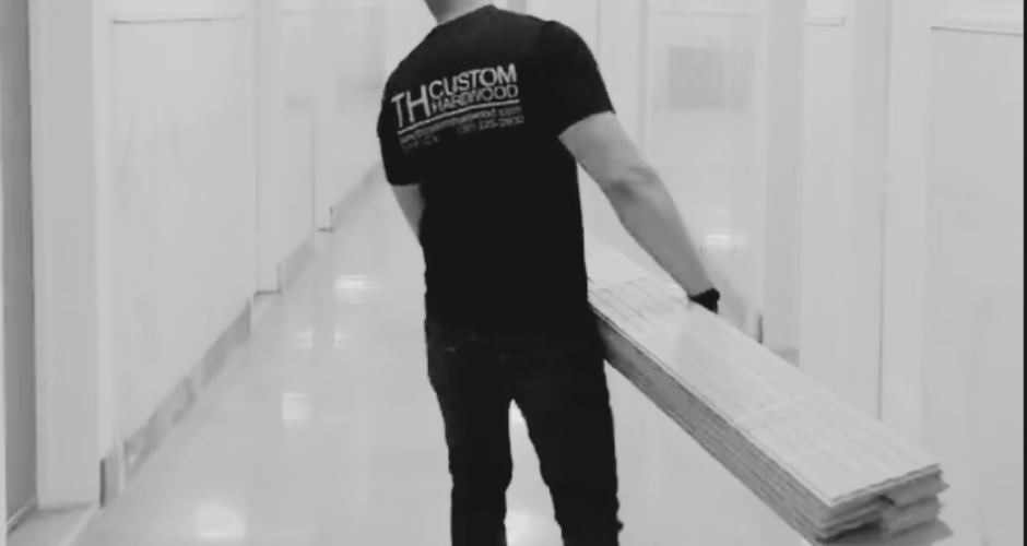Craftsman carrying custom hardwood planks down a hallway, representing precision workmanship and premium hardwood flooring installation.